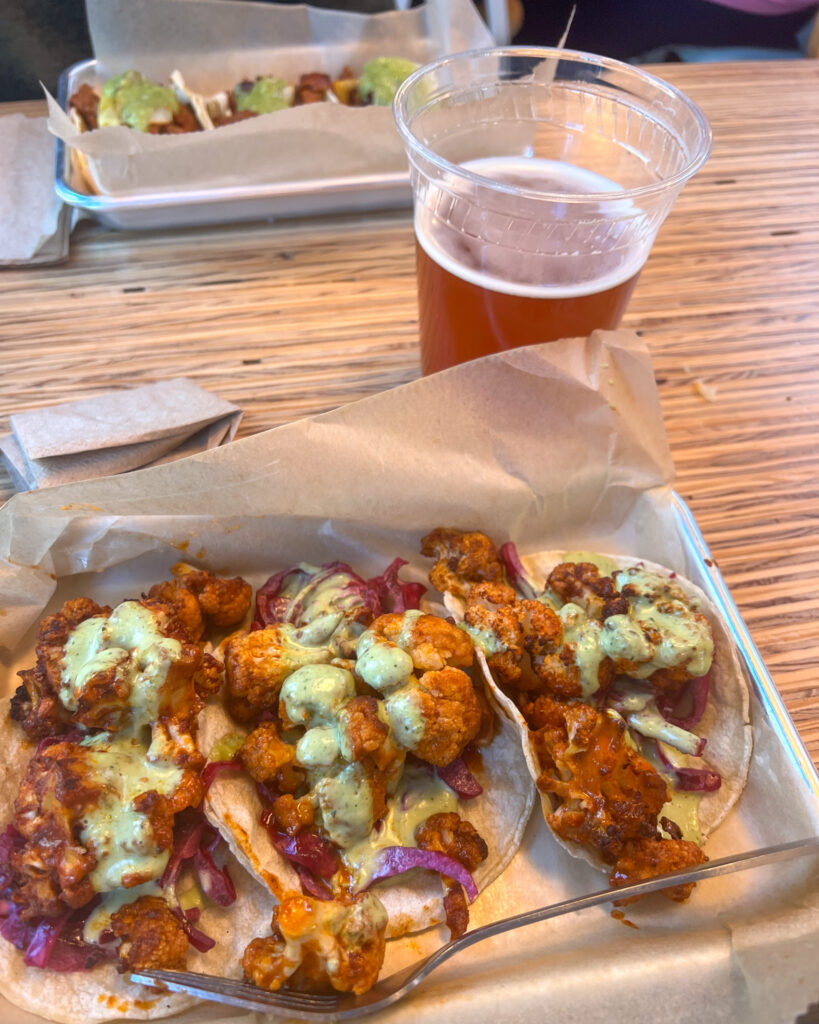 buffalo cauliflower bright orange with a light green sauce oured over top on a corn tortilla amber beer in the backgroun
